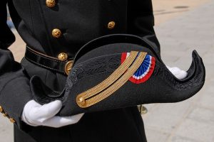 photographie d'un bicorne de Polytechnique tenu par deux mains gantées de blanc