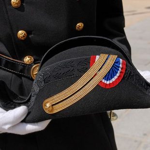 photographie d'un bicorne de Polytechnique tenu par deux mains gantées de blanc