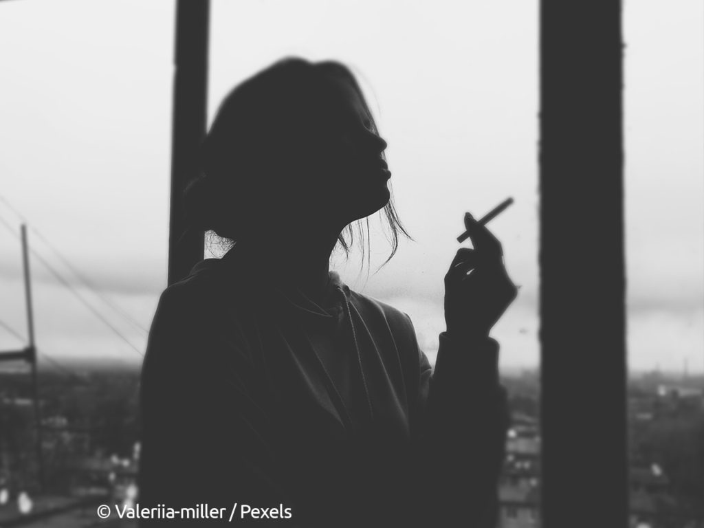 photographie en noir et blanc d'une femme à contrejour en train de faire une pause avec une cigarette