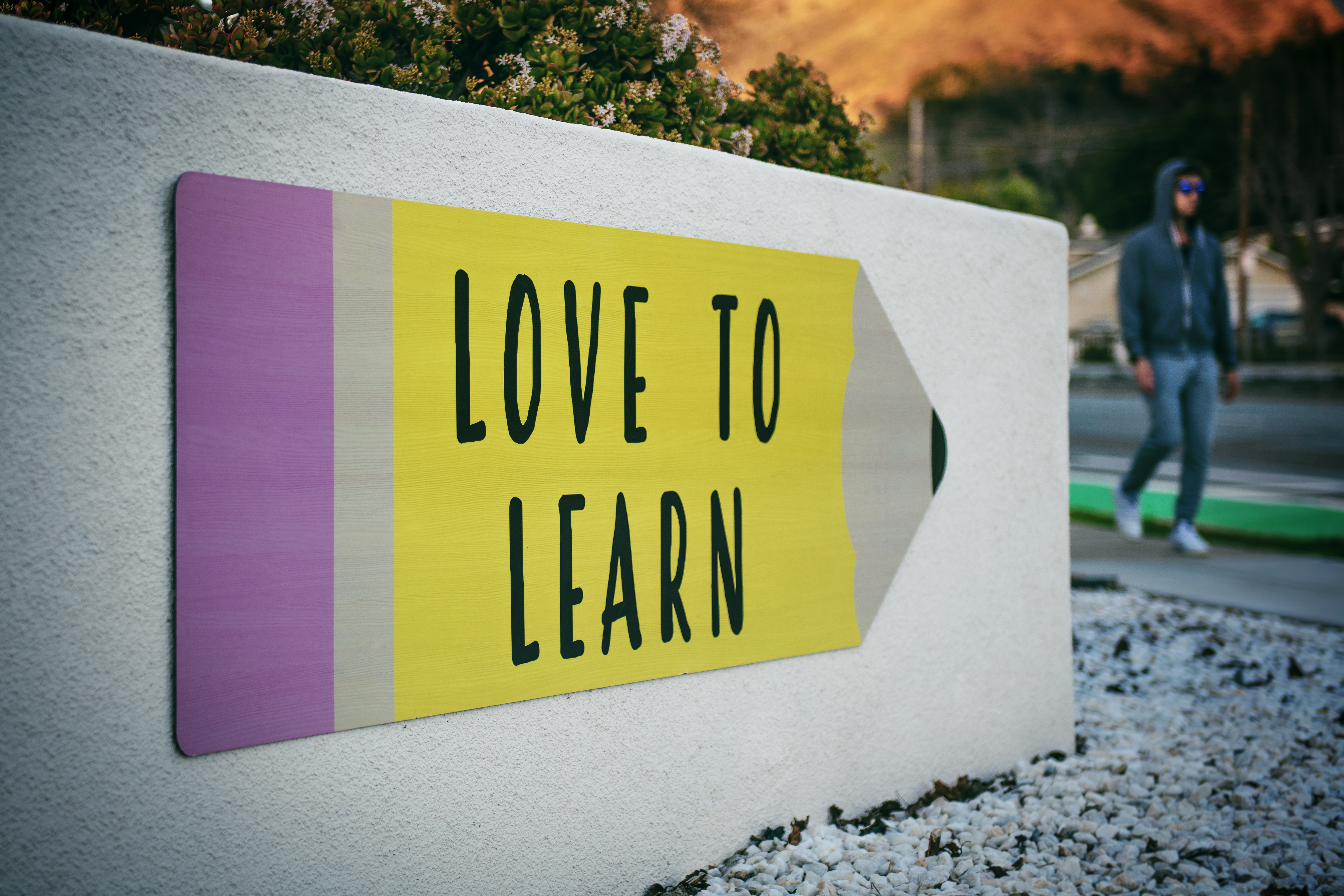 Panneau en forme de crayon "love to learn" avec un homme marchant à côté