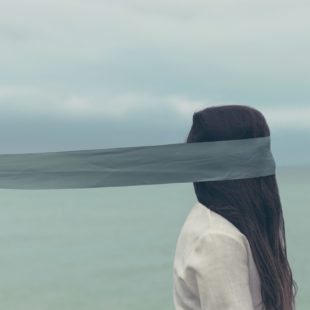 Face à la mer, une femme avec les cheveux qui retombent devant son visage et un ruban autour des yeux