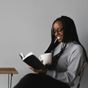 Femme assise en train de lire un livre une tasse à la main.