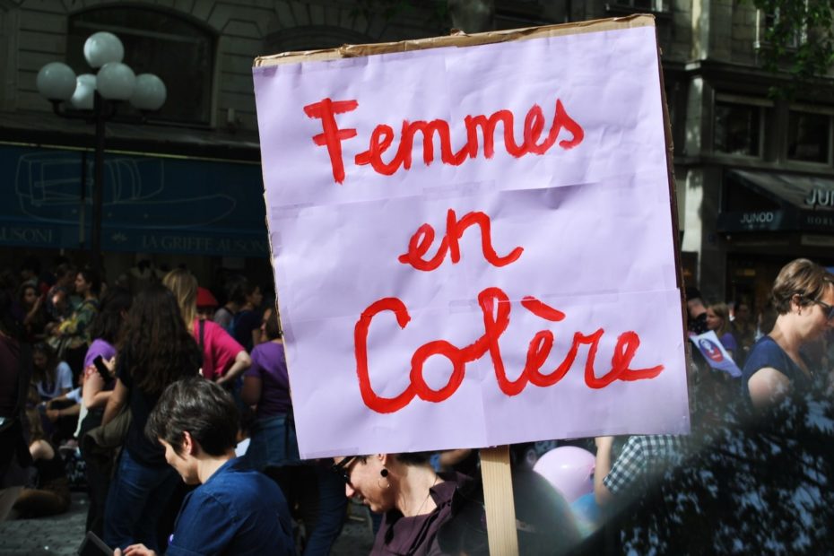 Manifestation de femmes dans une rue. Au premier plan est brandie une pancarte sur lequel est inscrit Femmes en colère