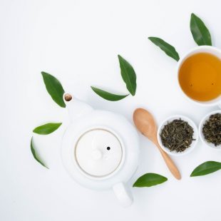 tasse de thé avec quelques feuille de thé verts autour
