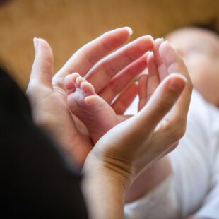 En amorce silhouette de femme, plan sur ses mains et arière-plan flou sur le bébé