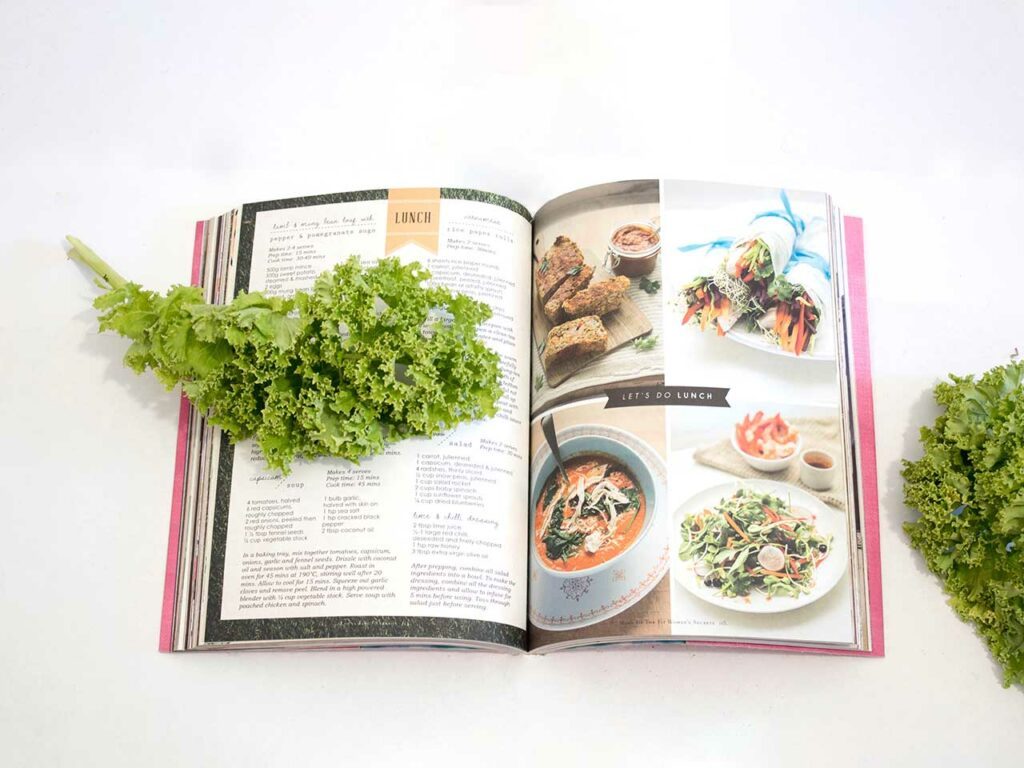 Photographie en couleurs et en format paysage d'un llivre de cuisine posé à plat sur un plan de travail. 2 feuilles de salade complètent la composition.